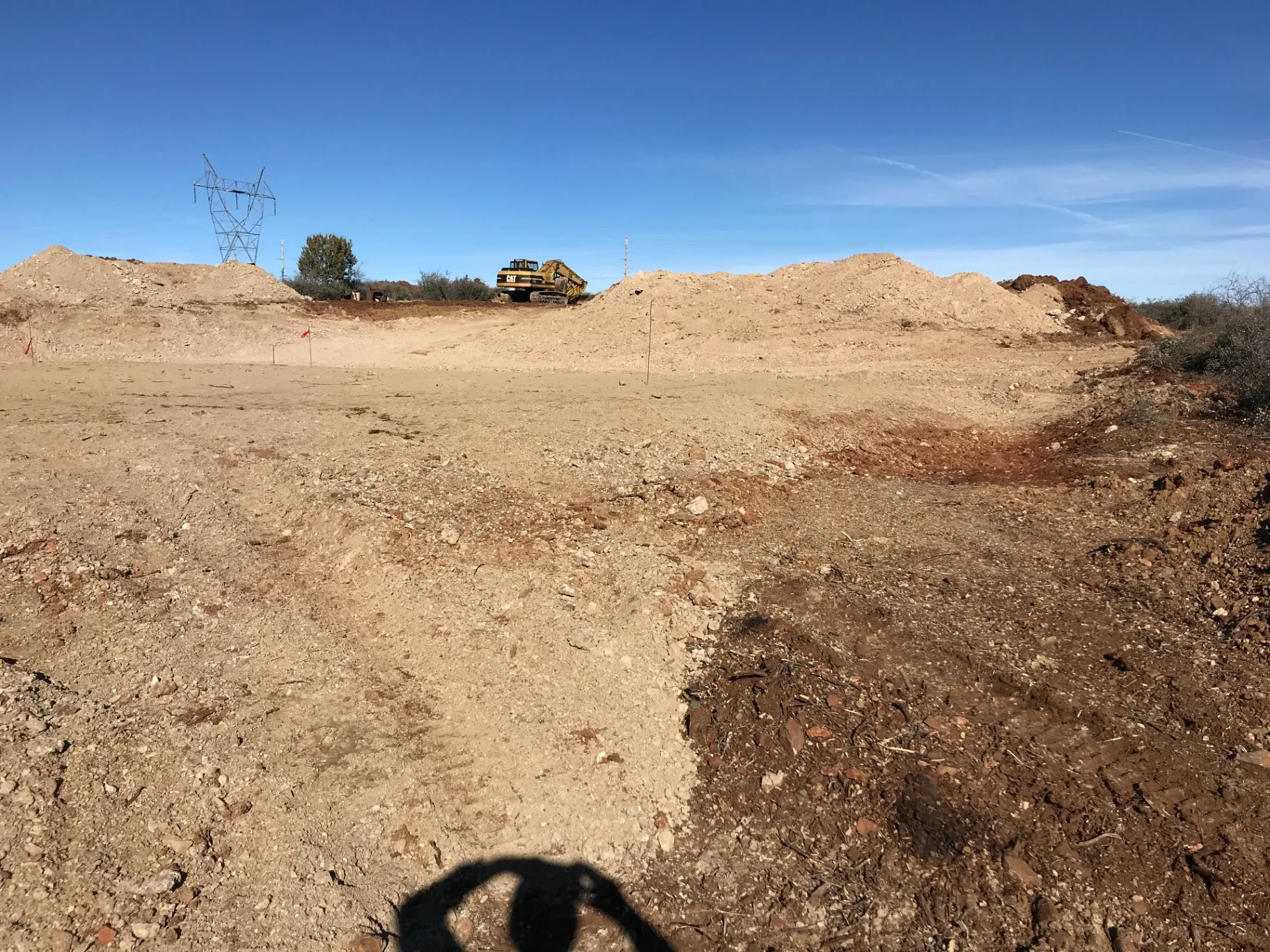 Building pad cut to finish grade on a North Phoenix lot with the pad edges staked and spoil stockpiled clear of the footprint